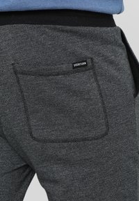 Grå joggers i texturerad tyg, med en bakficka med svart söm och en liten etikett med texten "YOURTURN." Elastisk midja synlig.