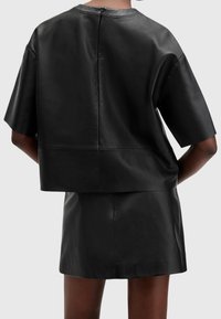Top corto in pelle nera con maniche corte, caratterizzato da un design minimalista, zip sul retro e una trama liscia. Abbinamento con una gonna coordinata.