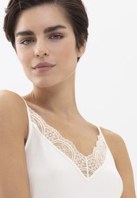 Creme camisole met kantafwerking en V-hals ontwerp. Glad stoftextuur en delicate bloemenkantaccenten langs de halslijn.