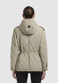 Gequilted beige jack met een capuchon, een riem op de taille, knoopmanchetten en een cirkelvormige logo-accent op de rug. Glad oppervlak.