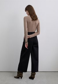 Top beige de manga larga combinado con pantalones negros de pierna ancha y cintura alta, con adornos laterales, y botas marrones de tacón. Diseño sencillo y ajustado.