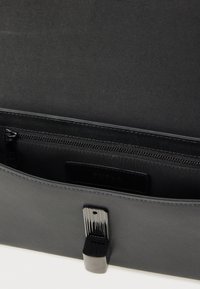 Melnas ādas soma ar teksturētu virsmu, kurā ir rāvējslēdzēja nodalījums un metāla aizdares detaļa. Iekšpusē ir gluda oderējuma.