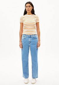 Gestreepte oranje en witte top met korte mouwen, gecombineerd met lichtblauwe rechte jeans en witte sneakers. De stof lijkt zacht met een casual pasvorm.