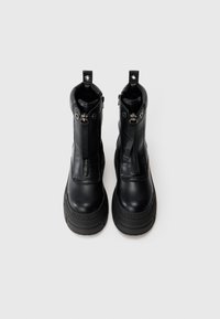 Botas de tornozelo em couro preto com fecho de rutura, sola texturizada e marca gravada na lateral. Acabamento suave com detalhes em hardware resistente.