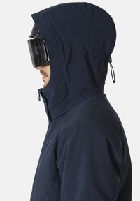 Tmavě modrá bunda s přiléhavou kapucí, zdobená předním zipem a texturovanou tkaninou. Spárovaná s černou lyžařskou maskou a brýlemi.