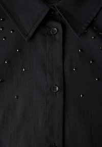 Una camicia nera button-up con una trama liscia, arricchita da piccole paillettes nere e un design con colletto classico.