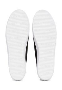 Paire de baskets noires vues par le dessous, avec des semelles en caoutchouc blanches embossées du logo "Tommy Hilfiger".