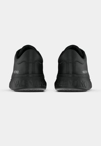 Chaussures de sport noires avec une tige lisse, une forme arrondie et un col rembourré. Affichent la marque "VALENTINO" sur le talon et la semelle.