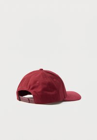 Tumši sarkana cepure ar izliekta lūpu, izgatavota no mīksta auduma, ar snapback regulēšanas iespēju un redzamām šuvēm aizmugurē.
