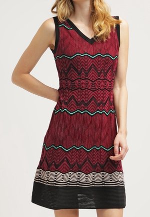 Ærmeløs rød kjole med sorte, grønblå og beige zigzag- og stribemønstre, med V-hals og knælængde.