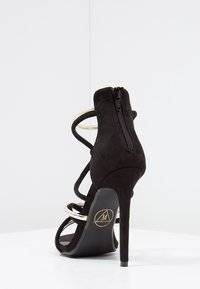 Sandale à talon haut en daim noir avec accents dorés, multiples brides et fermeture éclair à l'arrière. Semelle à texture lisse.