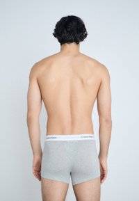 Boxers de algodón gris con cinturilla blanca que presenta el logo "Calvin Klein", vistos desde atrás contra un fondo claro.