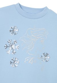 Sudadera azul claro con un perfil bordado en plata de una mujer y tres copos de nieve brillantes hechos de lentejuelas en la parte delantera.