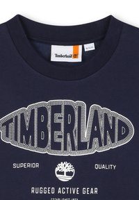 Felpa blu navy con scollatura a costine, caratterizzata dal logo "TIMBERLAND" ricamato in bianco, insieme a "SUPERIOR QUALITY" e un grafico di un albero sottostante.
