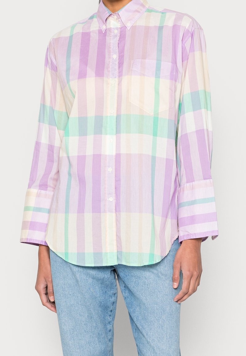 Chemise légère à carreaux avec boutons, en violet pastel, vert et crème. Elle présente des manches longues, une poche poitrine unique et un ourlet incurvé.
