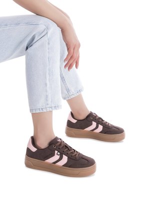Zapatillas de ante marrón con acentos en rosa y detalles de tres rayas, con un upper texturizado y suela de goma, llevadas con jeans de color azul claro.