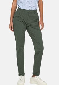 Chinos in cotone verde oliva con una vestibilità slim, dotati di passanti per la cintura, due tasche anteriori e texture del tessuto evidente. Abbinati a sneakers bianche.