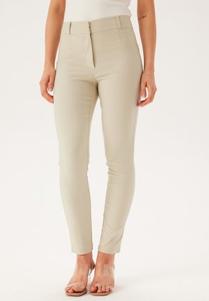 Beige kalhoty na míru s vysokým pasem, slim fit, hladkým povrchem a skrytým zipem, doplněné průhlednými sandály se šněrováním.