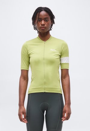 Άτομο που φοράει ανοιχτοπράσινο ποδηλατικό τζέρσεϊ με κοντά μανίκια και κουμπωτό φερμουάρ στο μπροστινό μέρος, μαζί με σκούρα γκρι επενδυμένα ποδηλατικά σορτς, στέκεται μπροστά σε λευκό φόντο.