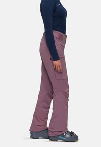 Purple ski pants with a water-resistant material, zippered pockets, and reinforced lower legs, paired with gray ski boots featuring accents.