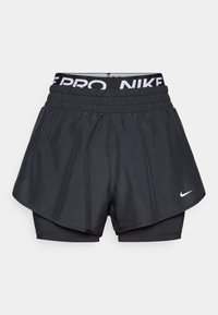 Mustat urheilushortsit, joissa on kerroksellinen malli ulkopuolisella kuorella ja sisäisillä kompressiohousuilla. Nike-logo vasemmalla puolella ja vyötärönauhassa.