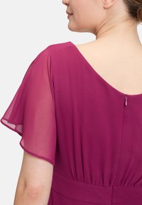Magenta Kleid mit transparenten Cap-Ärmeln, tiefem Rundrücken, zarten Raffungen an der Taille und einem kleinen Reißverschluss am Rücken.