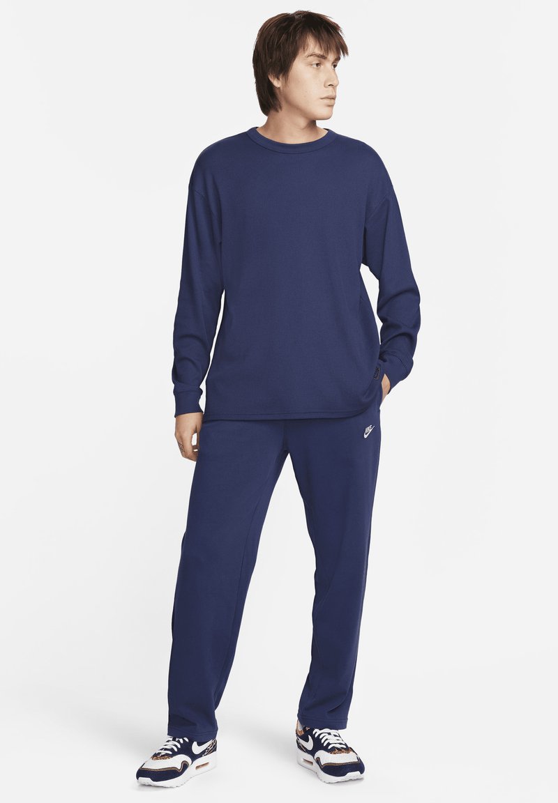 Chemise à manches longues bleu marine et pantalon de jogging assorti en tissu doux, avec une texture ribbed subtile et un petit logo.