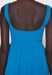 Blaues ärmelloses Kleid mit tailliertem, geripptem Oberteil und ausgestelltem Rock. Mit einem runden Rückenausschnitt und rotem "HUGO"-Logo über der Taille.