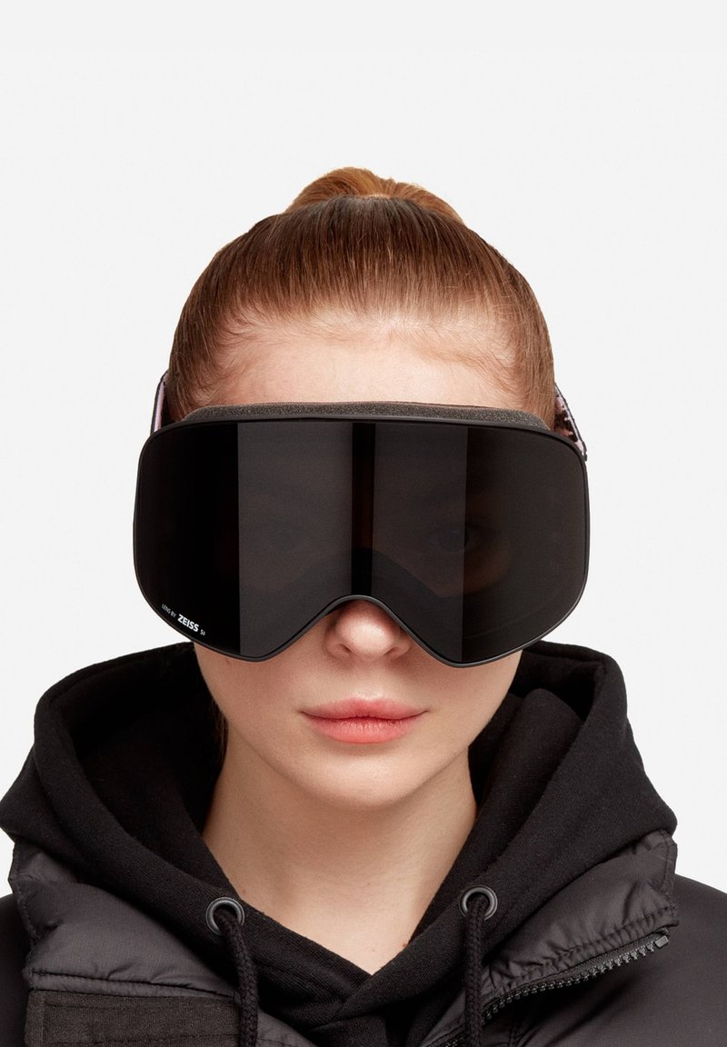 Gafas de esquí con una gran lente oscura y curvada, un marco de espuma negra suave y una correa ajustable con un patrón para un ajuste seguro.