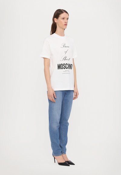 White cotton t-shirt featuring bold black text, paired with light blue denim jeans and black high-heeled shoes. Clean, minimalist design.