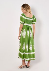 Grünes Leinenkleid mit kurzen Puffärmeln, gerafftem Oberteil und weißen dekorativen Mustern. Knöchellang, mit einem quadratischen Rückenausschnitt.
