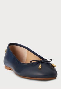 Sapatilha de balé em pele azul-marinho com bico arredondado, um pequeno laço e detalhes em metal dourado. Interior suave e sola plana castanha.