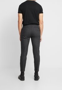 Grijze tweed broek met een slim fit, met een gladde textuur, twee achterzakken en opgerolde mouwen, gecombineerd met een zwart aansluitend T-shirt.