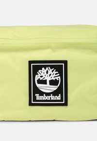 Sacchetto di tessuto giallo con un patch del logo Timberland in bianco e nero che presenta un albero e testo centrato sulla parte anteriore.
