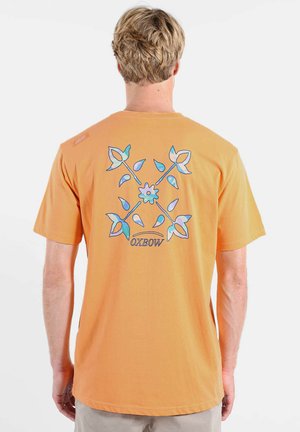 T-shirt en coton orange à manches courtes, avec un motif floral coloré dans le dos et une petite étiquette de marque sur l'épaule.