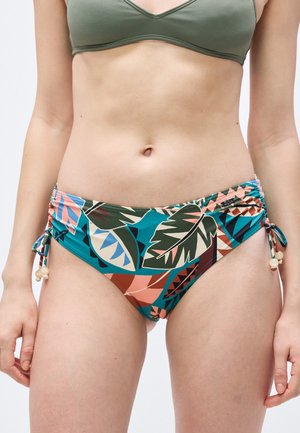 Femeie purtând top de bikini verde și chiloți de bikini cu imprimeu tropical colorat, cu șnururi reglabile pe lateral și detalii cu mărgele.