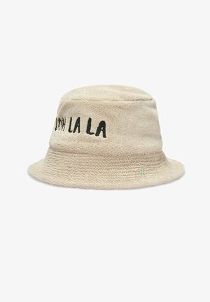 Chapeau bob beige texturé avec texte noir brodé "Ooh La La" sur le côté et un petit détail de trèfle vert près du bord.
