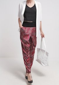 Röda byxor med paisleymönster och avslappnad passform, svart lager-på-lager topp, vit genomskinlig cardigan och en vit axelväska. Svarta balettflat-skor fulländar outfiten.