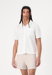 Chemise blanche texturée à manches courtes et col, avec un devant à boutons et une poche, assortie à un short beige clair.