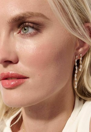 Guldøreringe med dråbeform, der har flere klare, glitrende krystaller arrangeret i et kaskadedesign. Den glatte, polerede overflade forbedrer glansen.