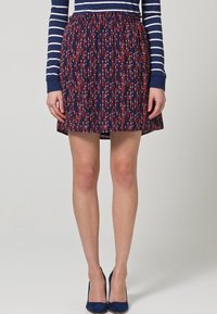 Jupe marine avec un motif à pois multicolores en rouge et bleu clair, dotée d'une taille élastique et d'un design évasé, atteignant le mi-cuisse.