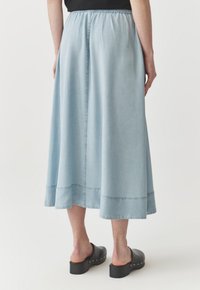 Svetlo modra jeans midi krila z elastičnim pasom, razširjeno obliko in surovim robom, v kombinaciji s črnimi platformskimi clogs.
