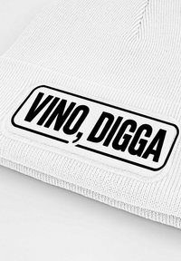 White knit beanie with a textured pattern and a rectangular black label displaying the text "VINO, DIGGA" in bold font.