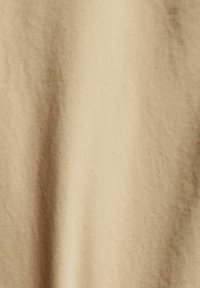 Tessuto beige con una superficie liscia e una leggera lucentezza, caratterizzato da pieghe e grinze sottili, che indicano morbidezza e capacità di cadere.