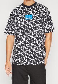 Svart kortärmad t-shirt med ett vitt geometriskt mönster och en blå fyrkantig bröstlogo. Tillverkad av bomullstyg har den en rundad halsringning.