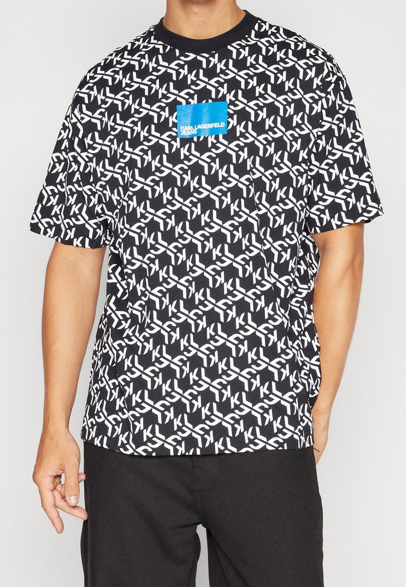 Svart kortärmad t-shirt med ett vitt geometriskt mönster och en blå fyrkantig bröstlogo. Tillverkad av bomullstyg har den en rundad halsringning.