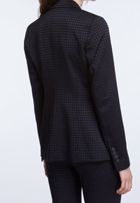 Blazer nero con un sottile motivo a scacchi. Presenta una vestibilità su misura, rever a intaglio e polsini con bottoni. Tessuto liscio e strutturato.