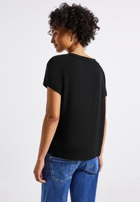 Haut noir à manches courtes avec une coupe décontractée, un col rond et une texture douce, assorti à un jean en denim bleu avec une coupe classique.