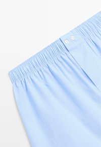 Shorts con fascia elastica azzurro chiaro a righe verticali sottili, con due chiusure a bottoni bianchi e texture liscia.