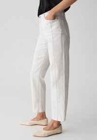 Pantaloni in denim bianco a gamba dritta con vita alta, dotati di tasche laterali e dettagli di cucitura a contrasto; abbinati a scarpe slip-on beige.